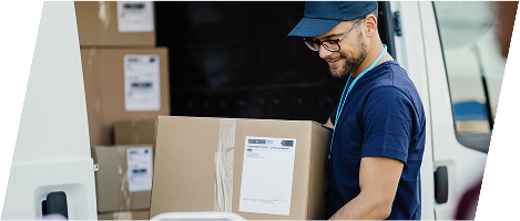 Ein freundlicher Paketbote mit Brille und Cap trägt einen großen Versandkarton aus einem Lieferwagen. Im Hintergrund sind weitere Pakete im Fahrzeug gestapelt. Die Szene vermittelt Professionalität, Zuverlässigkeit und modernen Paketdienst.