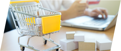 Symbolbild für Online-Shopping: Eine Person hält eine Kreditkarte in der Hand und tippt auf einem Laptop. Im Vordergrund steht ein kleiner Einkaufswagen sowie mehrere Miniatur-Versandkartons auf einem Holztisch. Die Szene stellt den E-Commerce-Prozess dar – von der Bestellung bis zum Versand.