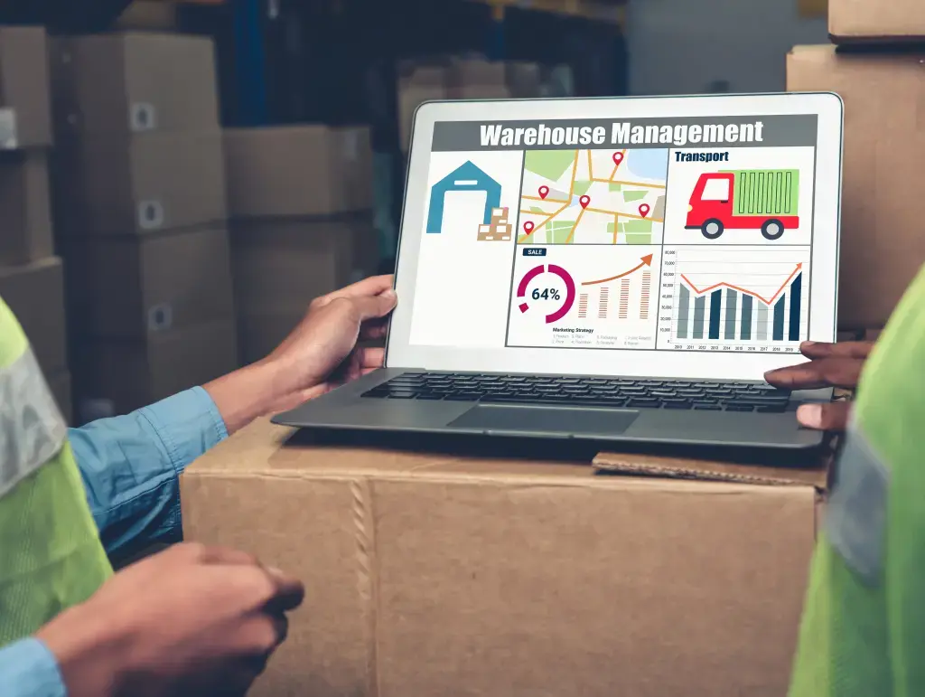 Zwei Mitarbeiter betrachten einen Laptop mit einem Dashboard zur Lagerverwaltung, das Diagramme, Transportdaten und Statistiken anzeigt.